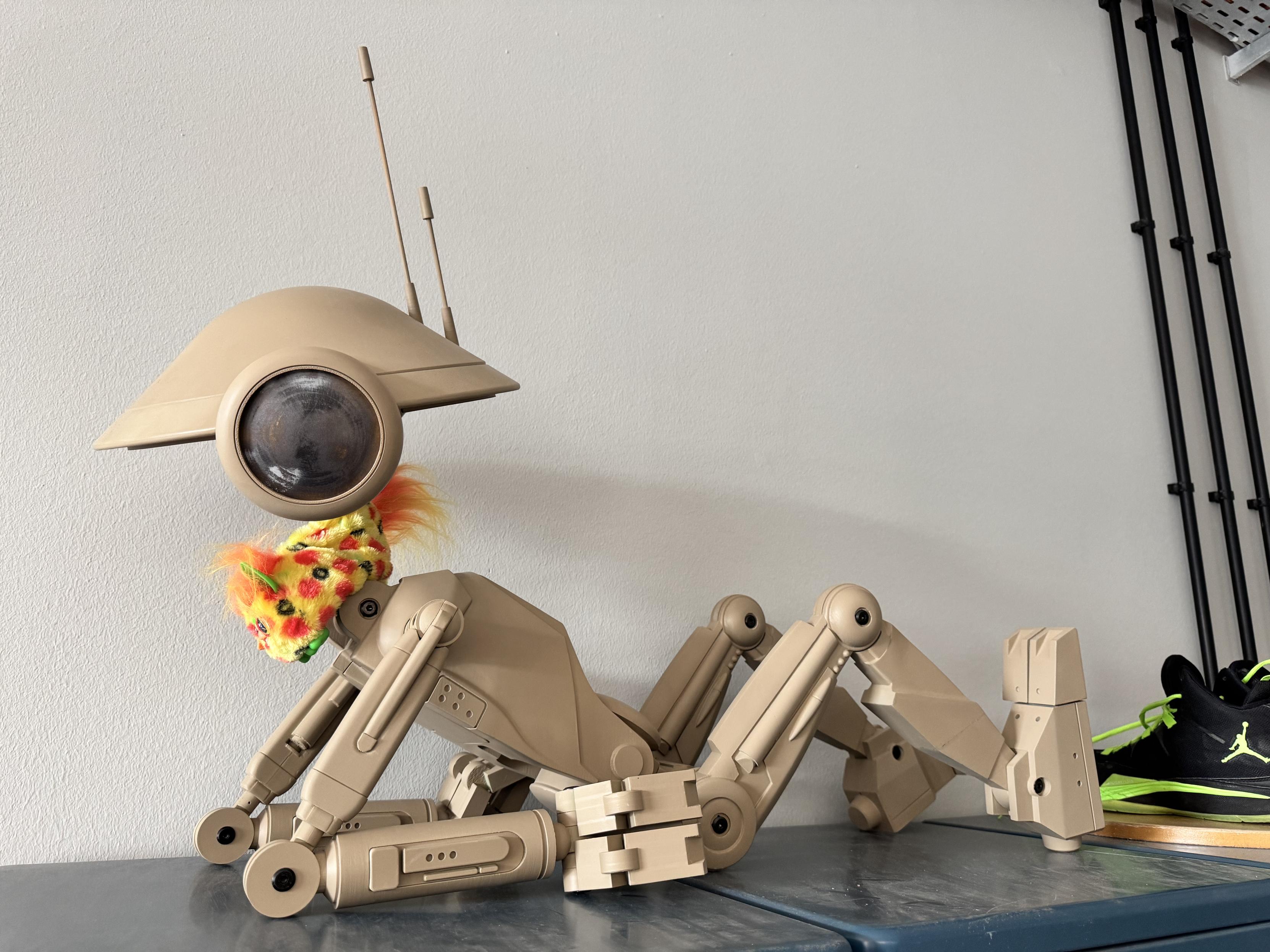 A 3D printed Star Wars pit droid in a sexy pose, with a modern long furby wrapped around its neck. Why? We don't know.