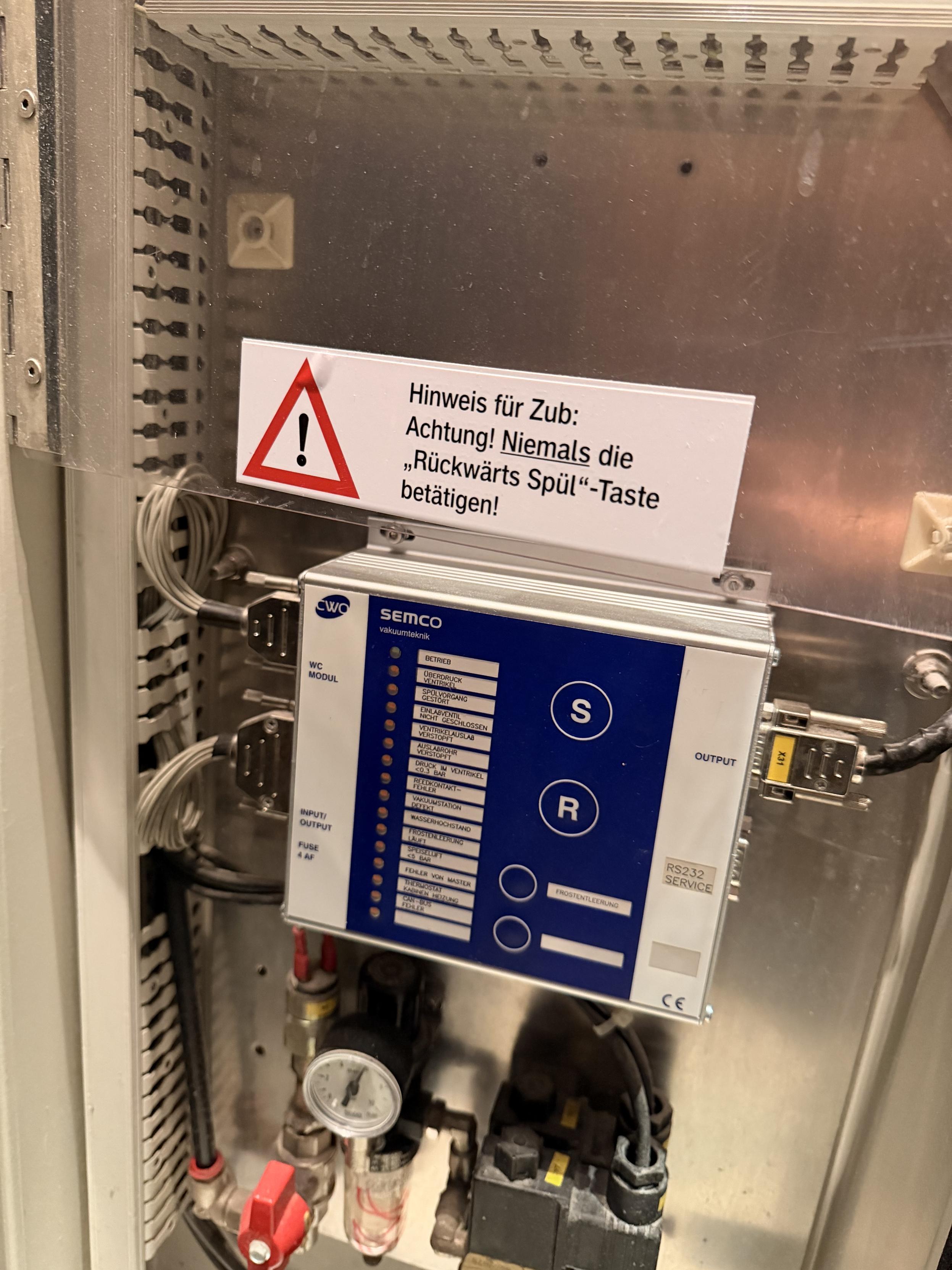 Foto von dem Technikschrank hinter dem Spiegel auf dem Zugklo. Typischerweise verschlossen, hier war er offen. Zu sehen ist eine Steuerungseinheit für das Spülsystem mit einem großen Warnhinweis: "Hinweis für Zub: Achtung! Niemals die »Rückwärts Spül«-Taste betätigen!"